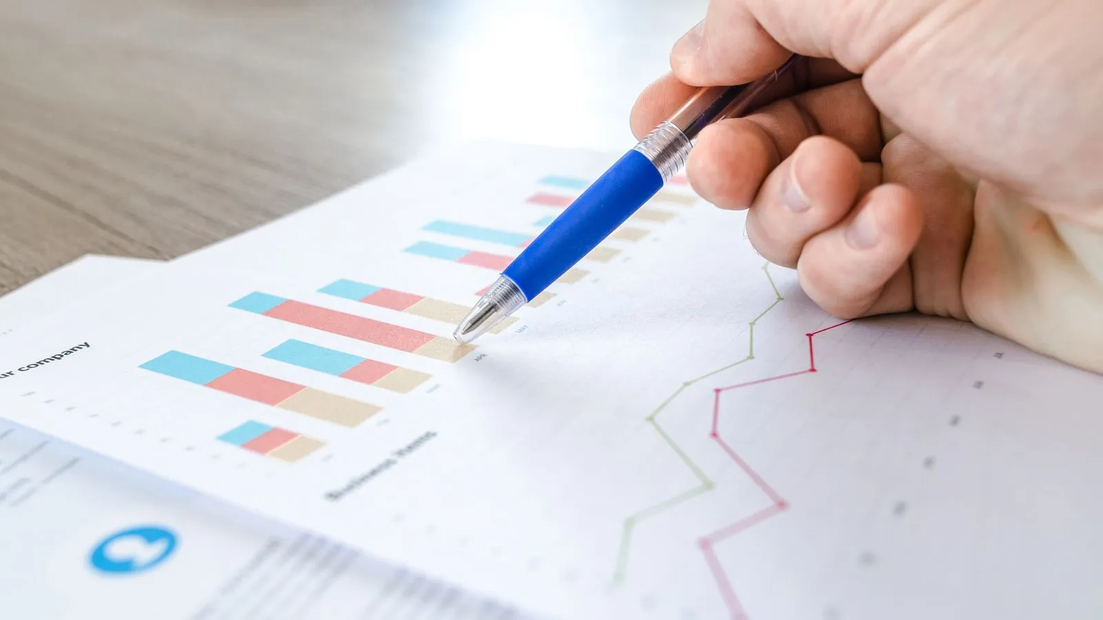 A hand with a pen reviewing colorful data charts and a spreadsheet on a desk
