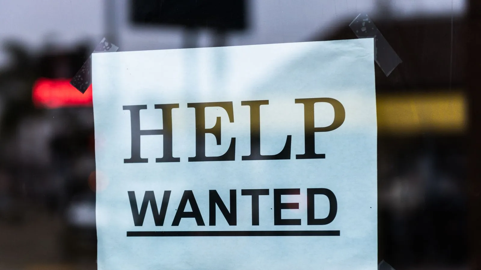 A 'Help Wanted' sign taped inside a storefront window