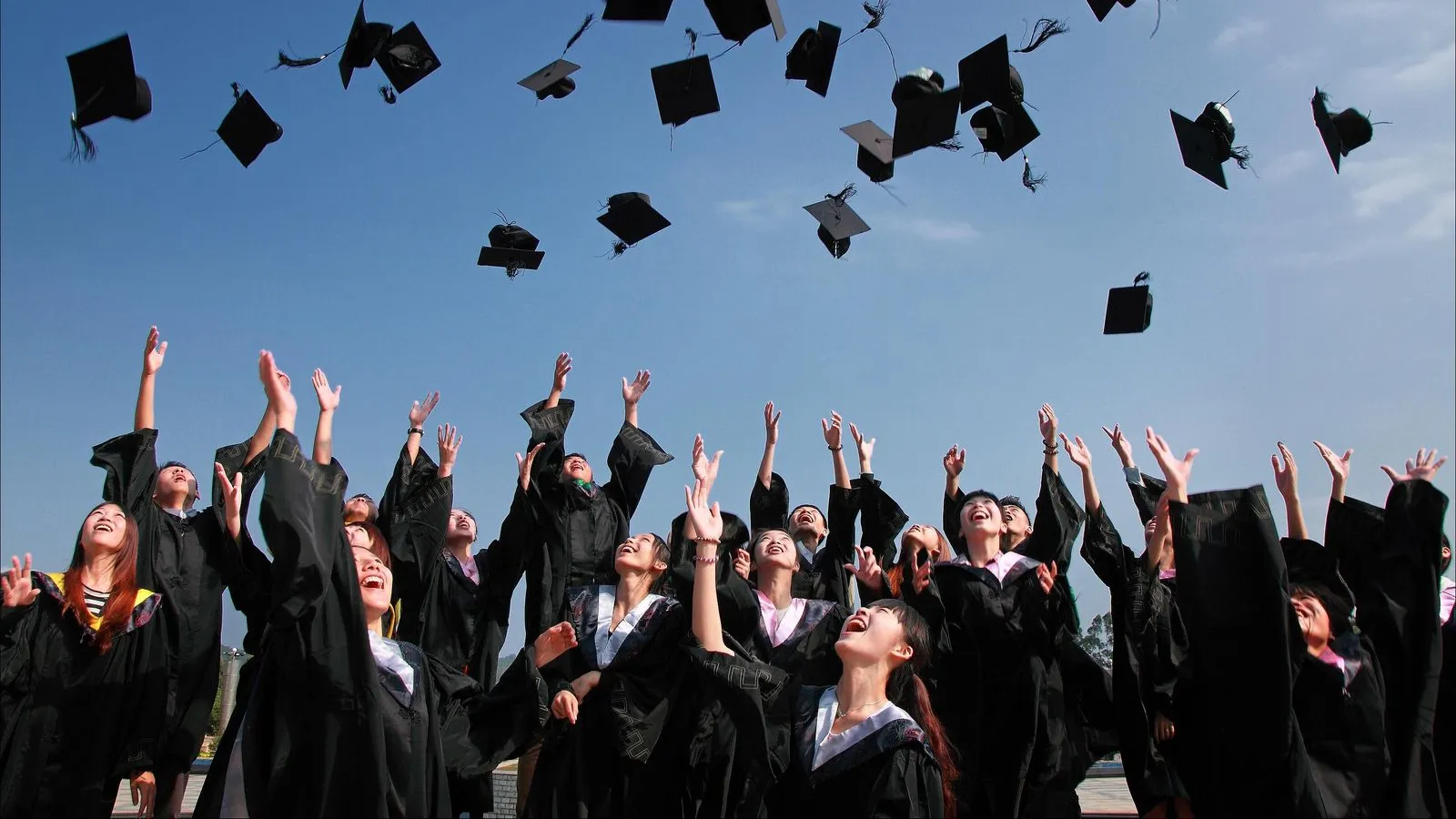 College graduates in caps and gowns throwing their mortarboards into the air